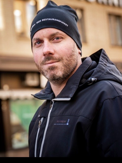 Victoria Jern Nilsson, Lokalvårdare Carl-Mikael (som kallas för Kalle) har en svart mössa och munkjacka med fackföreningens logotyp.