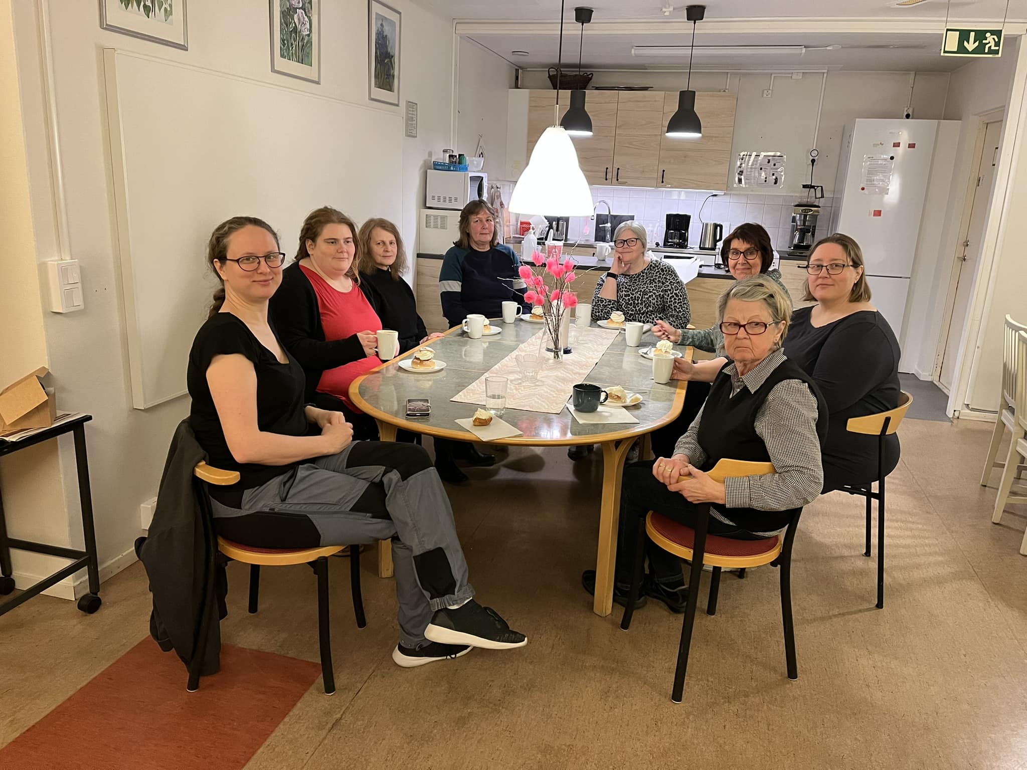 Bild på personer på kontoret runt ett bord. Alla har en semla framför sig då denna bild togs på fettisdagen