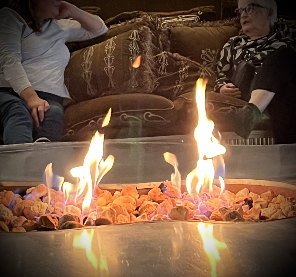 Två kvinnor sitter i en soffa och samtalar. I förgrunden brinner två små eldar.